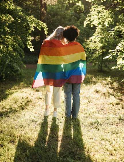 Two people standing in forest with rainbow flag wrapped around them