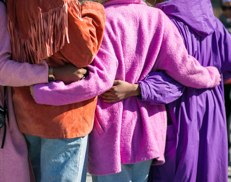 People with backs to camera in colorful coats with arms around each other