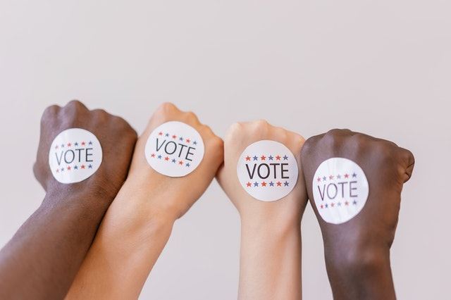 photo of hands of black people and white people with VOTE stickers on them