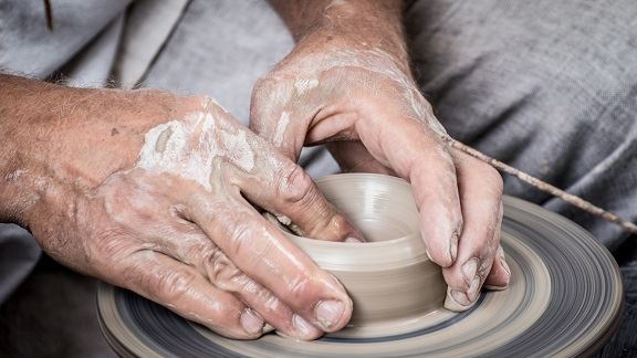 A pair of hands shaping clay on a potter's wheel.