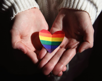 Cupped hands holding rainbow heart.